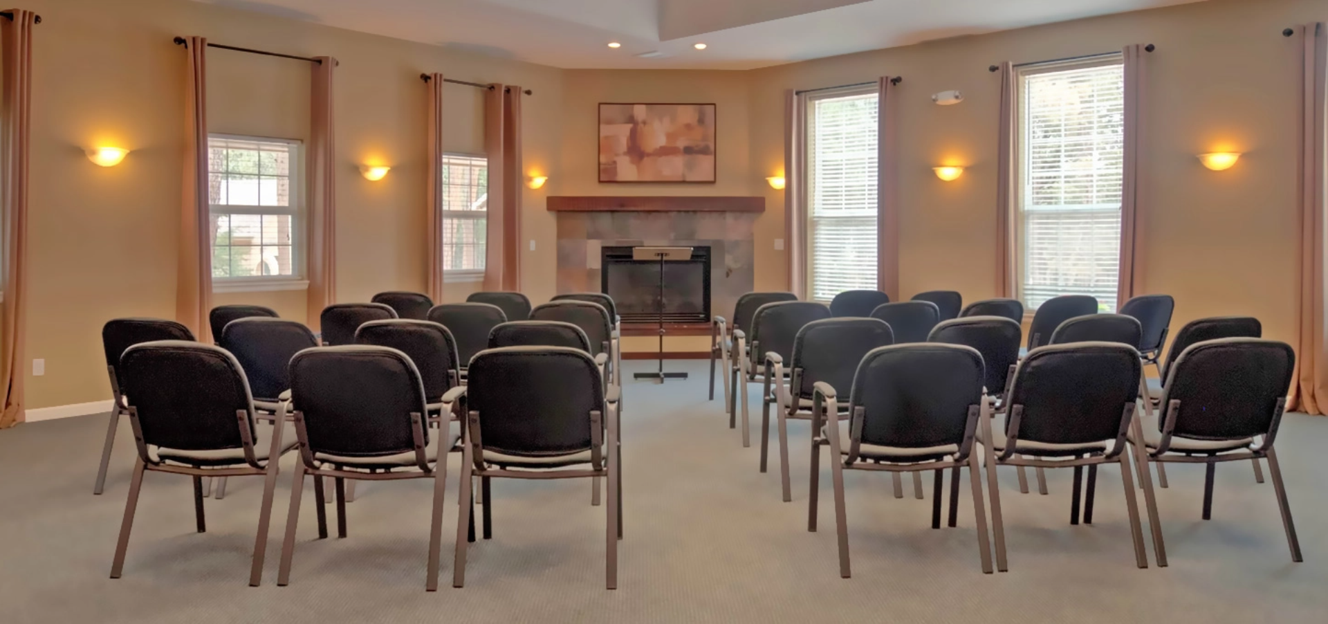 A meeting room with chairs arranged in rows, a fireplace, and windows.